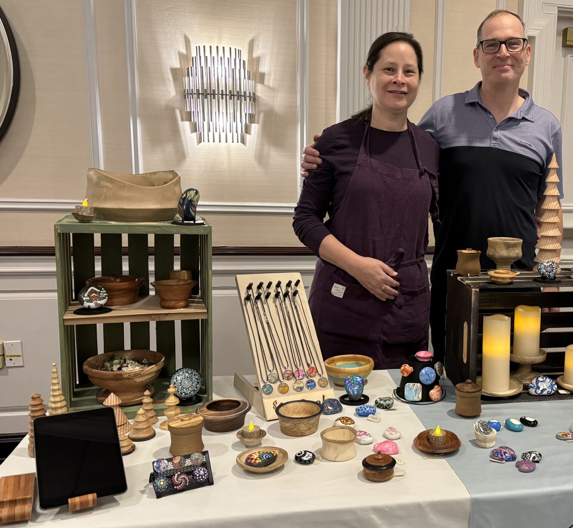 A man and woman stand beside a table displaying an assortment of items, engaged in conversation A man and woman stand beside a table displaying an assortment of items, engaged in conversation